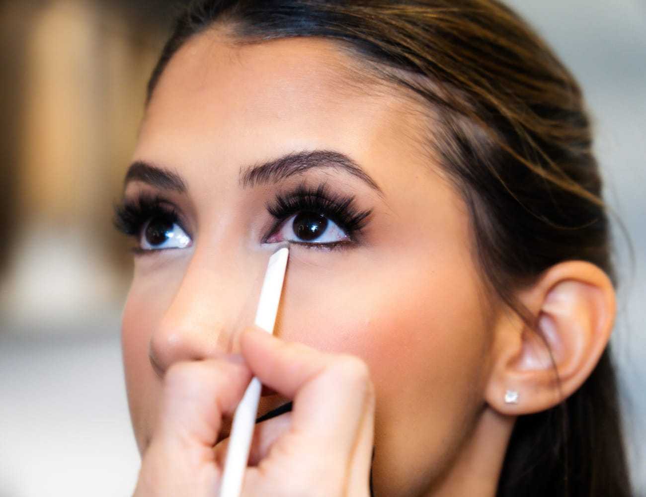 Makeup artist applying eyeliner to woman's eye.