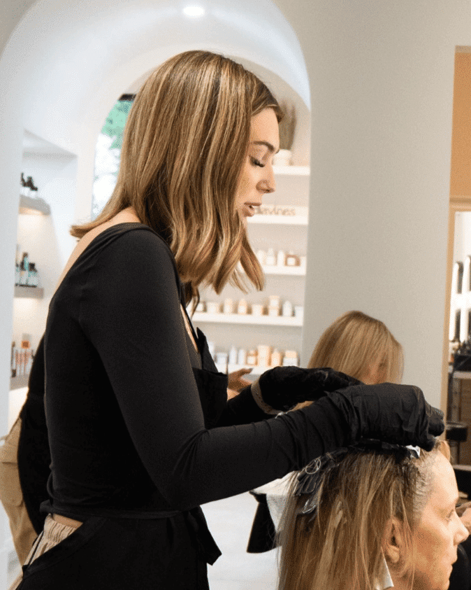 Hair stylist applying dye to a client's hair at a salon.