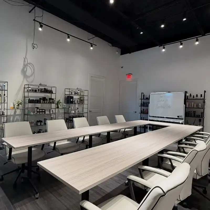 Modern conference room with long tables, white chairs, shelves, and a whiteboard.