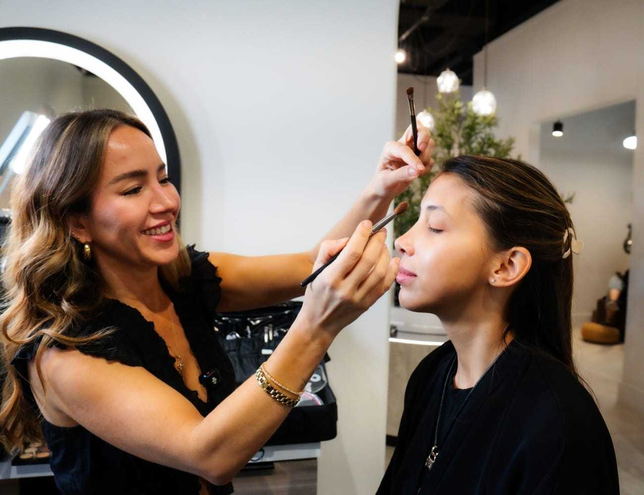 Makeup artist applying eyeshadow to a young woman in a salon setting.