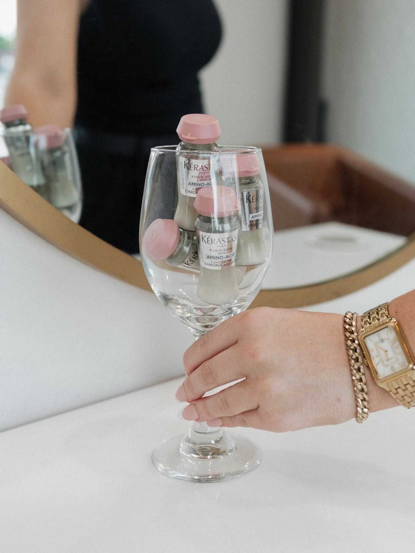 Kerastase hair products displayed in a wine glass on a mirrored table.