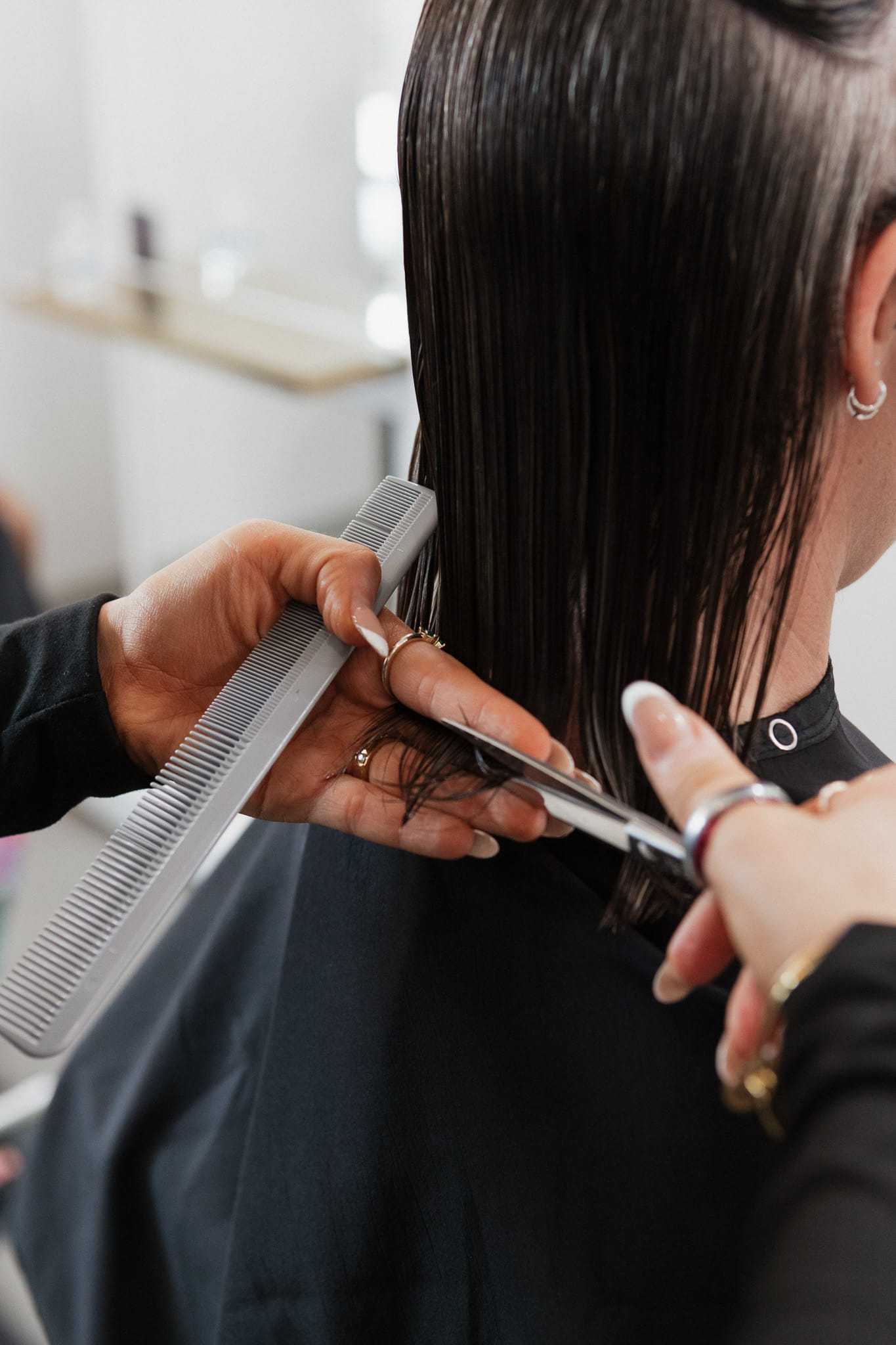 Hairdresser cutting straight brown hair with scissors in a salon.